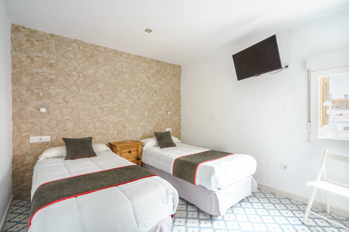 Una habitación con dos camas, una pared de piedra, un televisor y un piso con diseño.