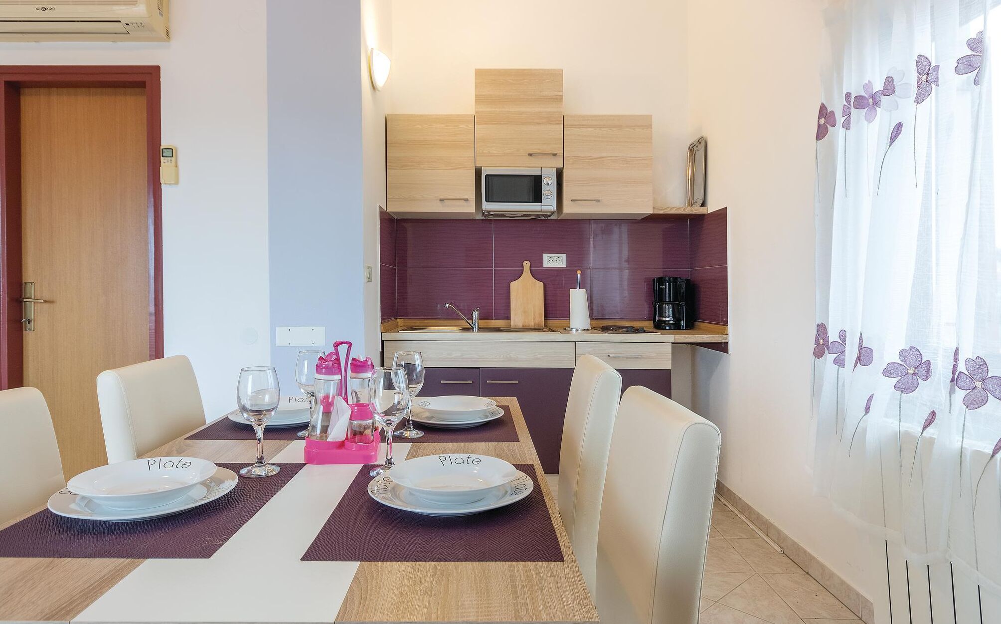 A dining area with a table set for four, a microwave, and a coffee maker in the kitchen.
