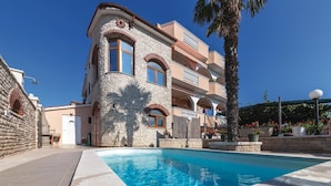 Un immeuble à plusieurs étages, doté d’une façade en pierre, d’une piscine et d’un palmier.