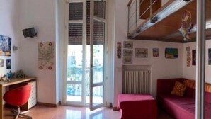 Une pièce avec un fauteuil rouge, un canapé rouge, un radiateur et une fenêtre avec des stores.