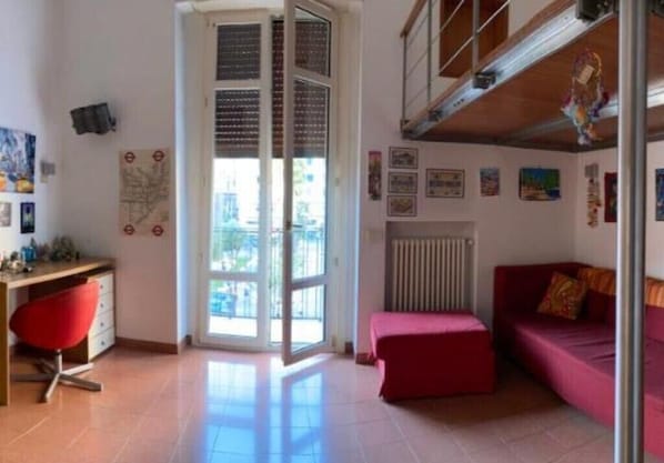 A room with a red chair, a red sofa, a radiator, and a window with blinds.