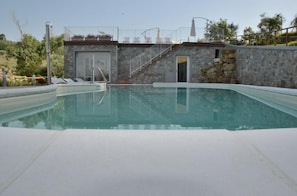 A swimming pool with a stone wall and a staircase leading to a door. - Podere delle Fanciulle (Pistoia)