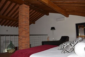 A bedroom with a brick pillar, a bed with zebra-patterned pillows, a black chair, and a floor lamp. - Podere delle Fanciulle (Pistoia)
