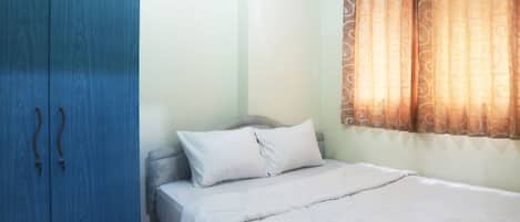 A bedroom with a bed, a wardrobe, and a window with curtains.