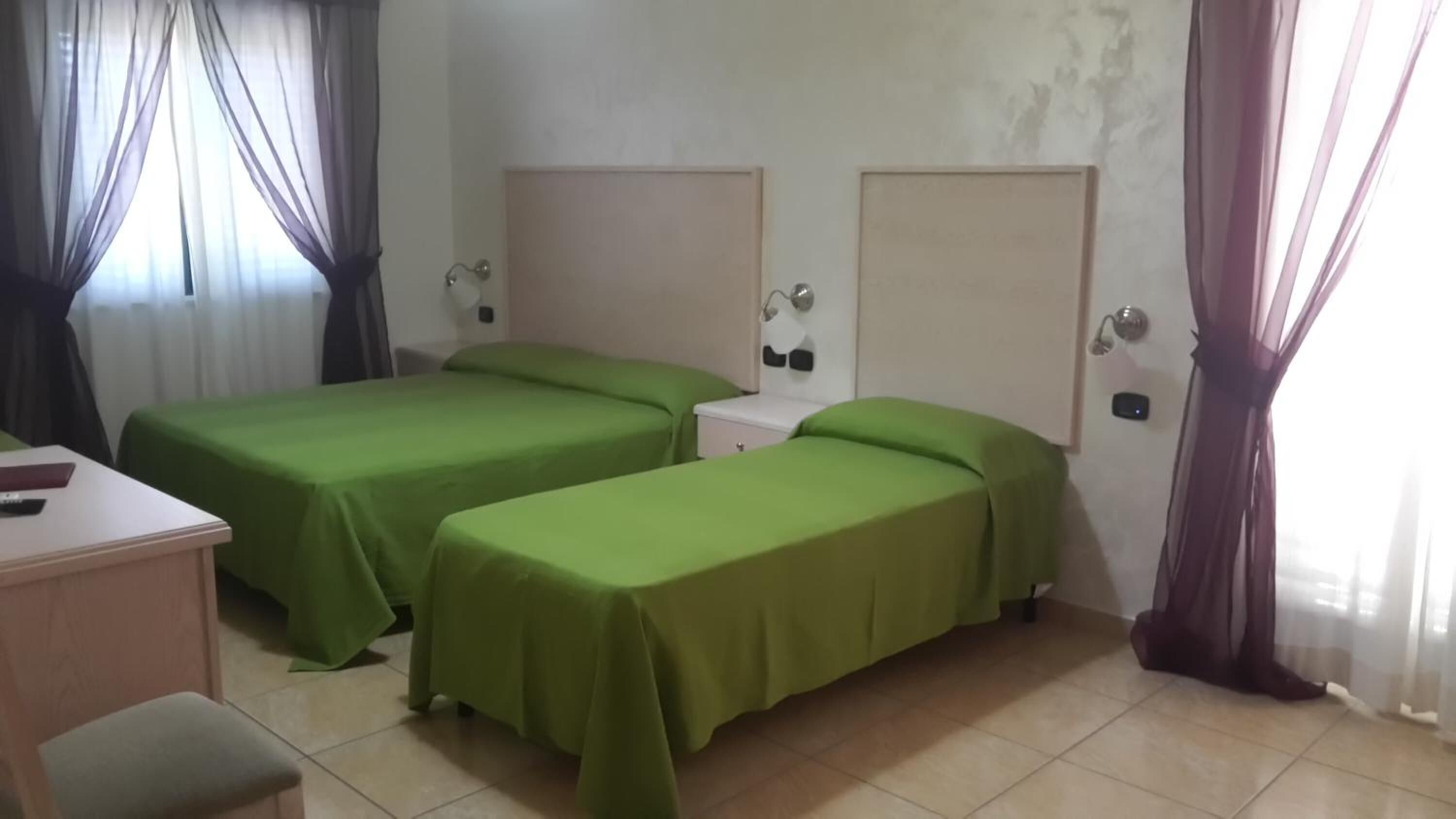 A hotel room with two single beds, a desk, a chair, and a bedside table.
