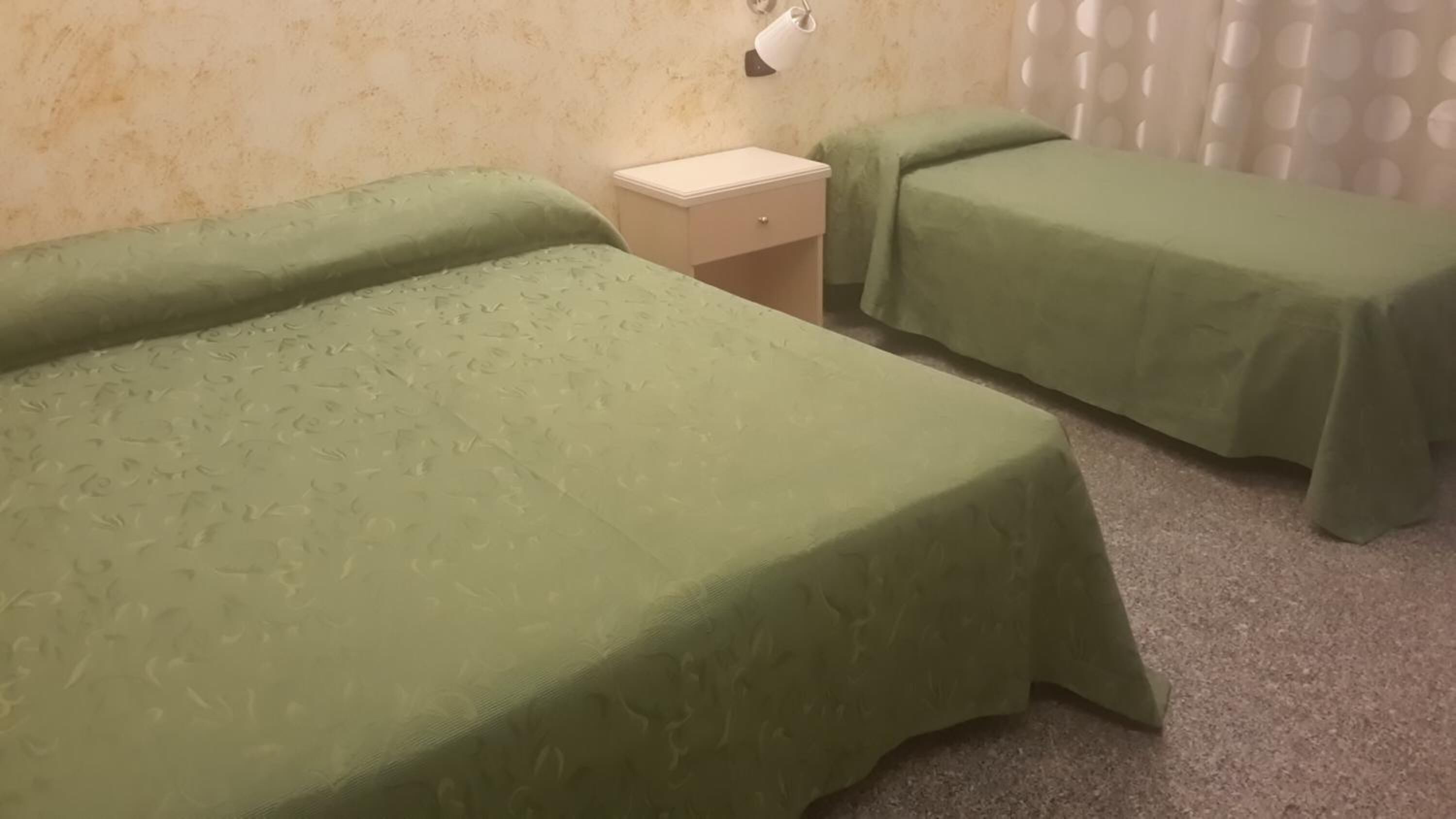 Una habitación con dos camas individuales, una mesita de noche pequeña y una lámpara fijada a la pared.