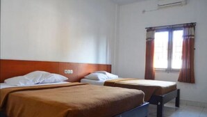 Two single beds with wooden headboards in a room with white walls and a window with curtains. - Hotel Nuansa Indah (Denpasar)