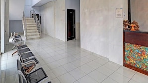 A spacious hallway with a staircase, a row of chairs, and a reception area with a decorative panel. - Hotel Nuansa Indah (Denpasar)