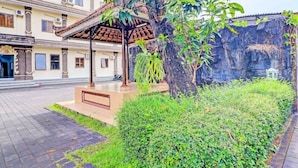 A gazebo with a tiled roof, surrounded by lush greenery and a stone wall. - Hotel Nuansa Indah (Denpasar)