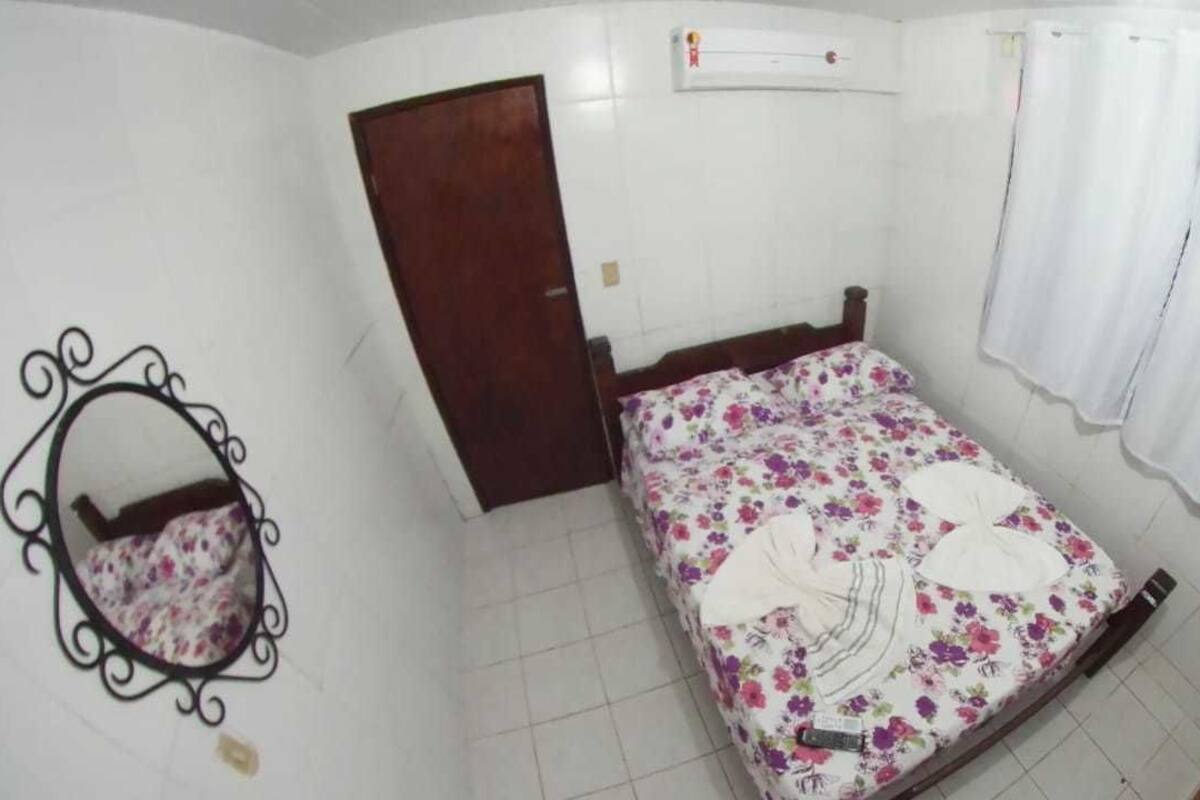 A bedroom with a bed, a wooden door, a white air conditioning unit, and a white curtain.