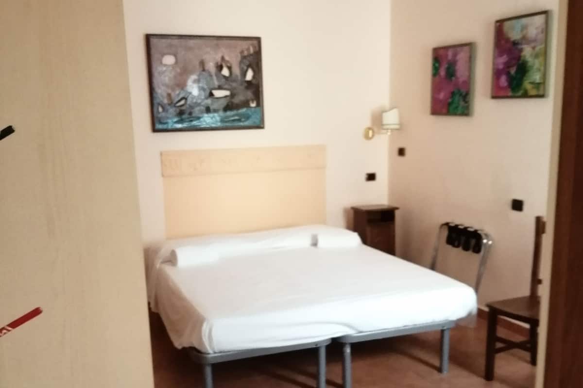 A bedroom with a bed, a chair, a wall-mounted air conditioner, and a painting.
