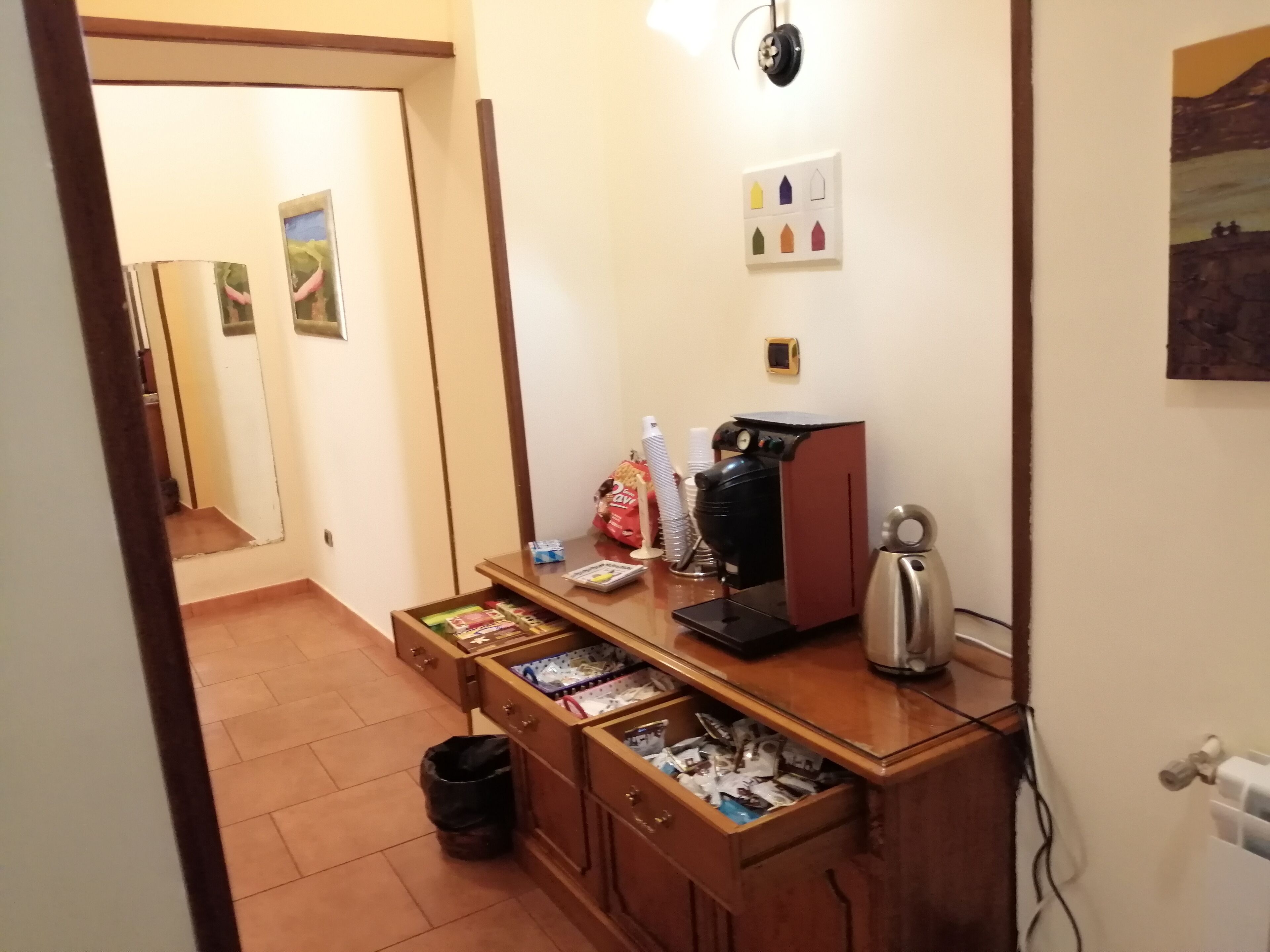 Una kitchenette pequeña con una cafetera, un cubo de basura y un cajón con varios objetos.