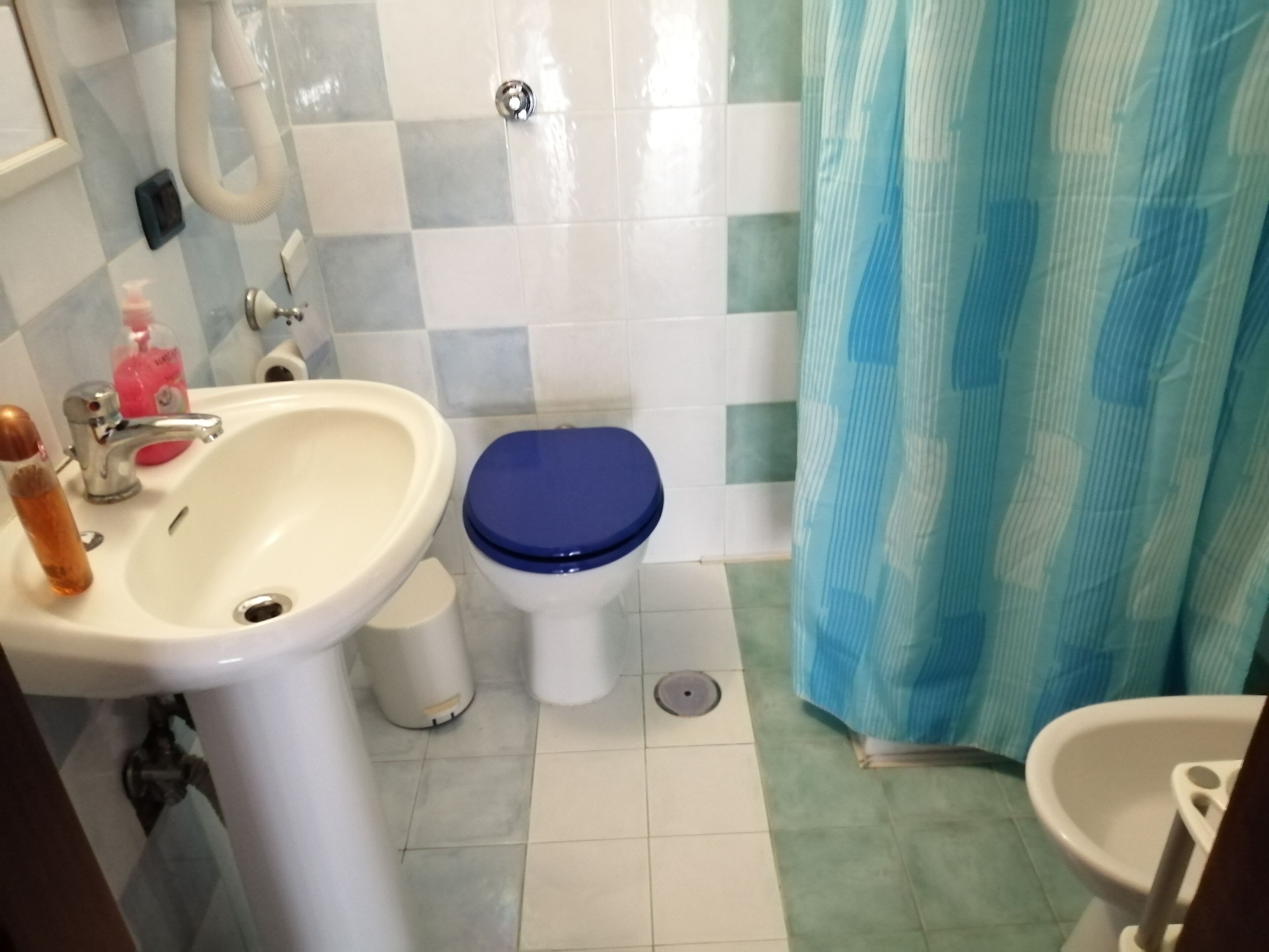A bathroom with a white sink, a blue toilet, and a shower curtain.
