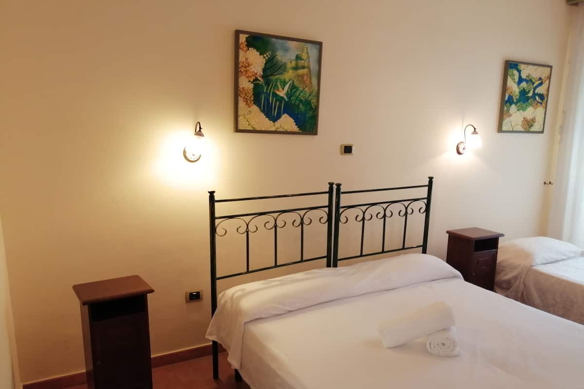 A bedroom with two beds, each with a white bedspread and pillows. There are wall-mounted light fixtures on either side of the beds.
