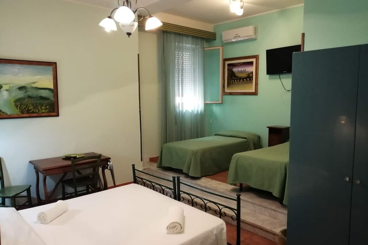 A hotel room with two beds, a desk, a chair, a wardrobe, and a ceiling light fixture.