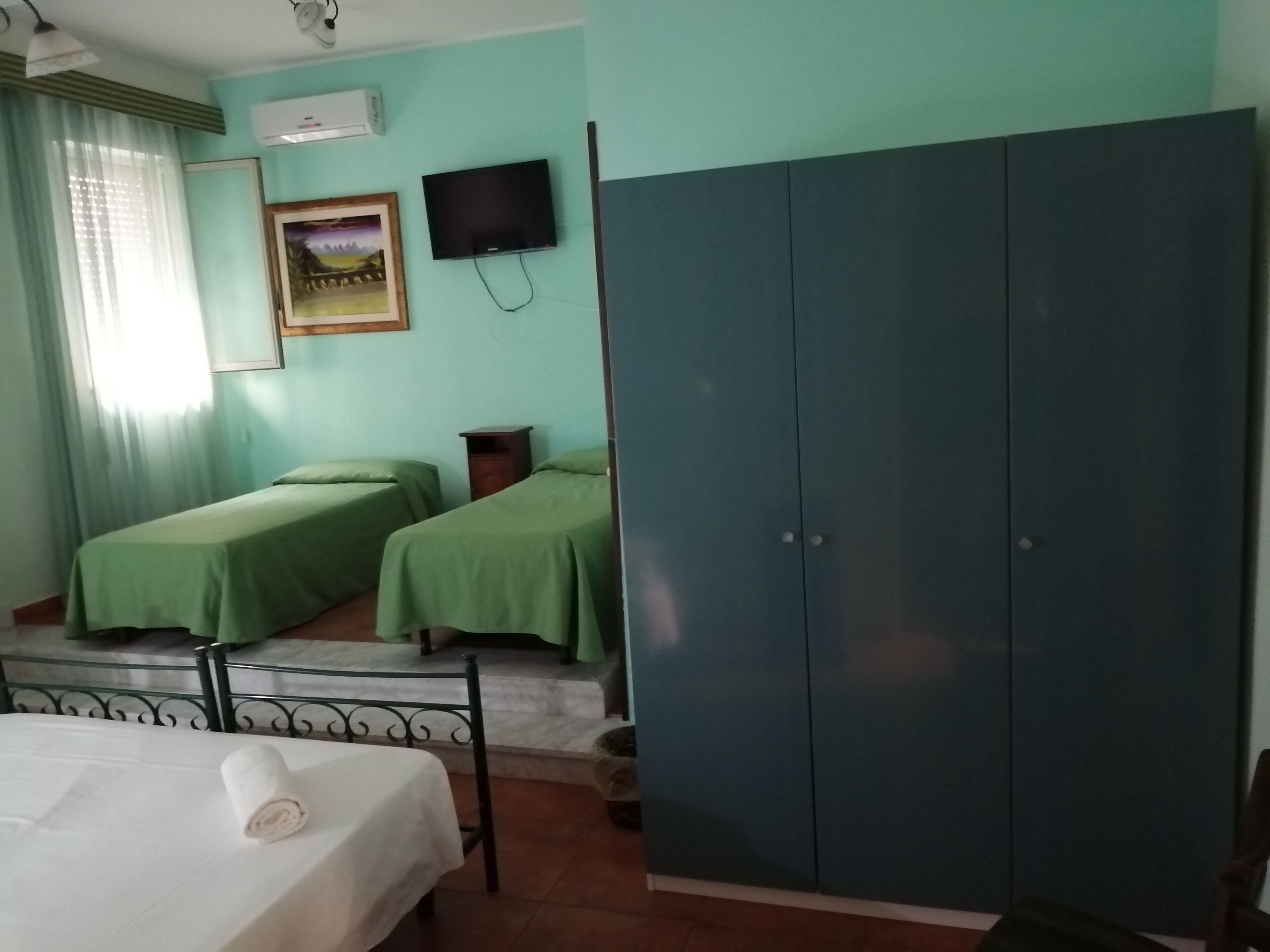A room with two single beds, a large wardrobe, a television, and a window with curtains.
