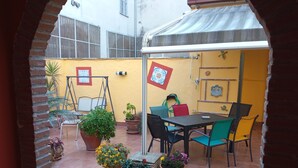 Uma área de pátio com mesa e cadeiras, rodeada por plantas em vasos.