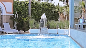 Una piscina con fuente, rodeada de sillas de descanso y follaje.