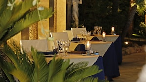 Un área de comedor al aire libre con mesas dispuestas para una comida, con velas y cristalería transparente.