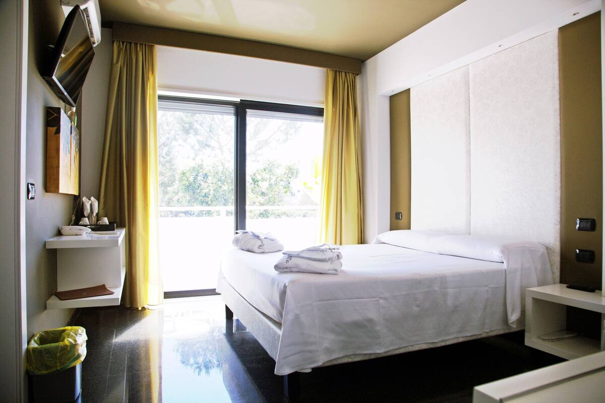 A hotel room with a bed, a bedside table, a TV, and a window with curtains.