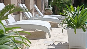 Zona de piscina con sillas reclinables blancas y plantas en macetas.