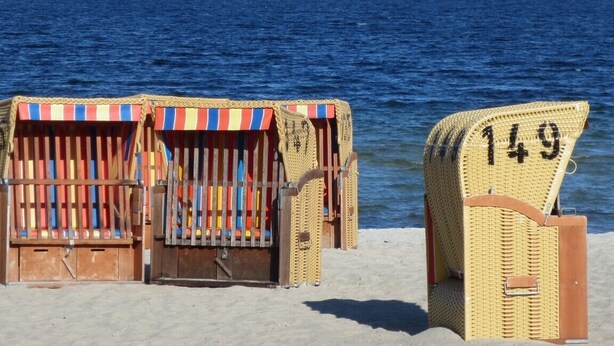 Beach chairs with numbers, a sandy beach, and a view of the sea with boats in the distance. - Mediterranean lifestyle in a historic setting  (Luhnstedt)