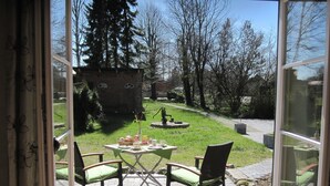 An outdoor patio with a table set for two, surrounded by chairs, overlooking a grassy yard with trees and a brick structure in the background. - Mediterranean lifestyle in a historic setting  (Luhnstedt)