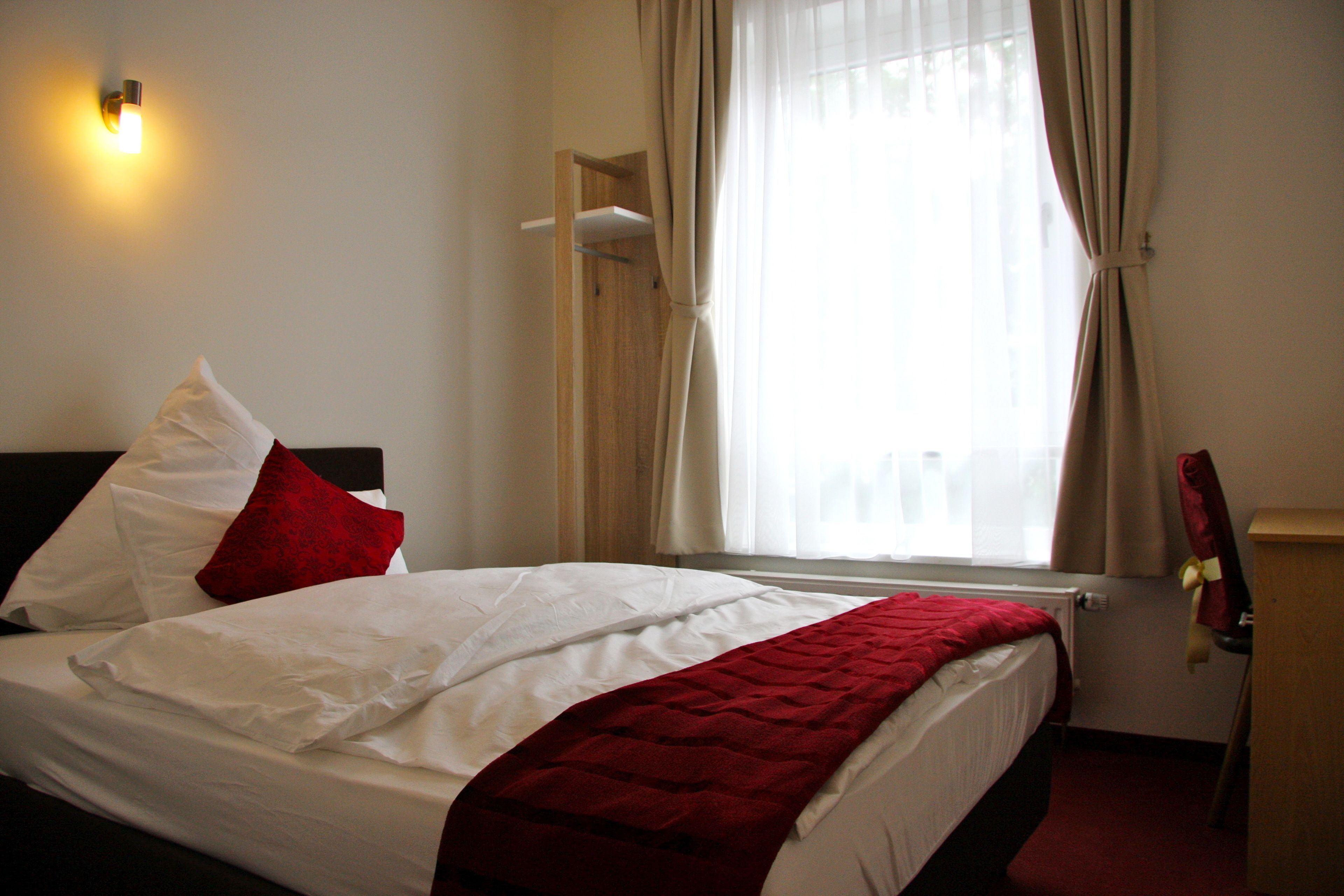 Ein Hotelzimmer mit Bett, Nachttisch, Lampe und einem Fenster mit Vorhängen.