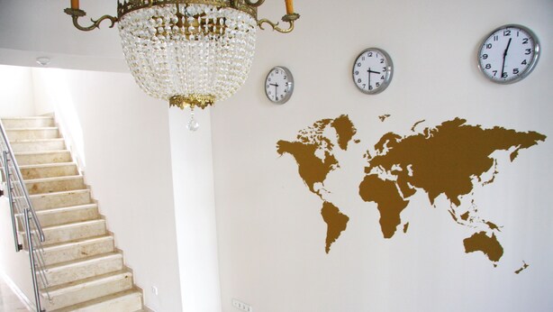 A staircase with a chandelier, three clocks, and a world map on the wall. - Hotel Gemini (Düsseldorf)