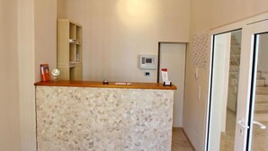 A reception area with a mosaic-tiled counter, a wooden cabinet, a thermostat, and a door leading to a staircase. - Hotel Gemini (Düsseldorf)