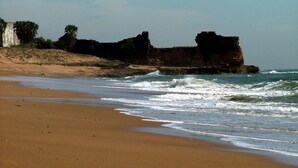 A sandy beach with waves crashing onto the shore and a large rock formation in the background. - Dream Vision Guest House (Diu)