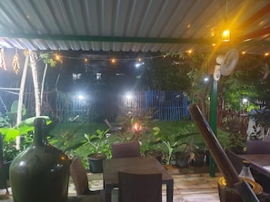 An outdoor patio area with a covered seating area, potted plants, and a small fire in the background. - Dream Vision Guest House (Diu)