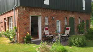 A brick building with a green door, two chairs, and a table outside. - App. Morniglight, flooded by the sun (Luhnstedt)