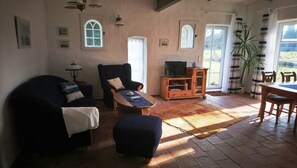 Un salon comprenant un canapé, un fauteuil, un pouf, une table basse en bois, un meuble pour la télévision et une table à manger avec des chaises.