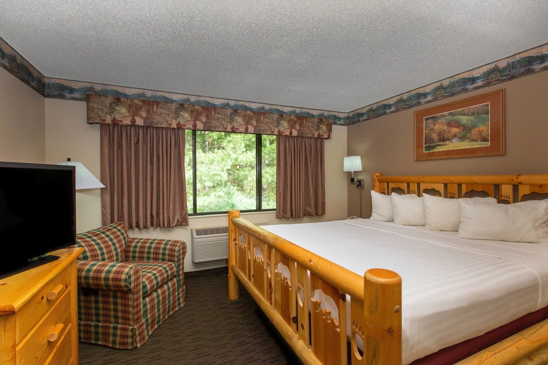 A hotel room with a large bed, a television, a plaid sofa, and a painting on the wall.