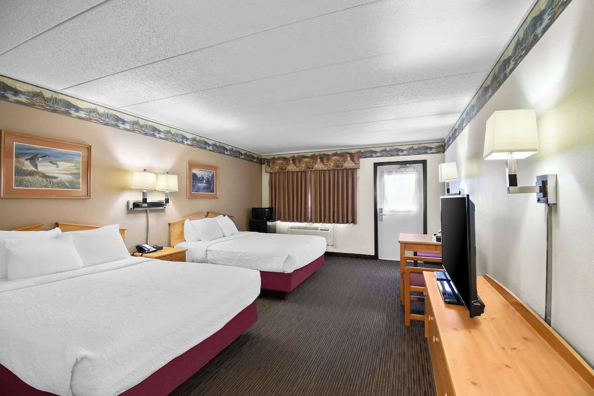 A hotel room with two beds, a desk, a TV, and a window with curtains.