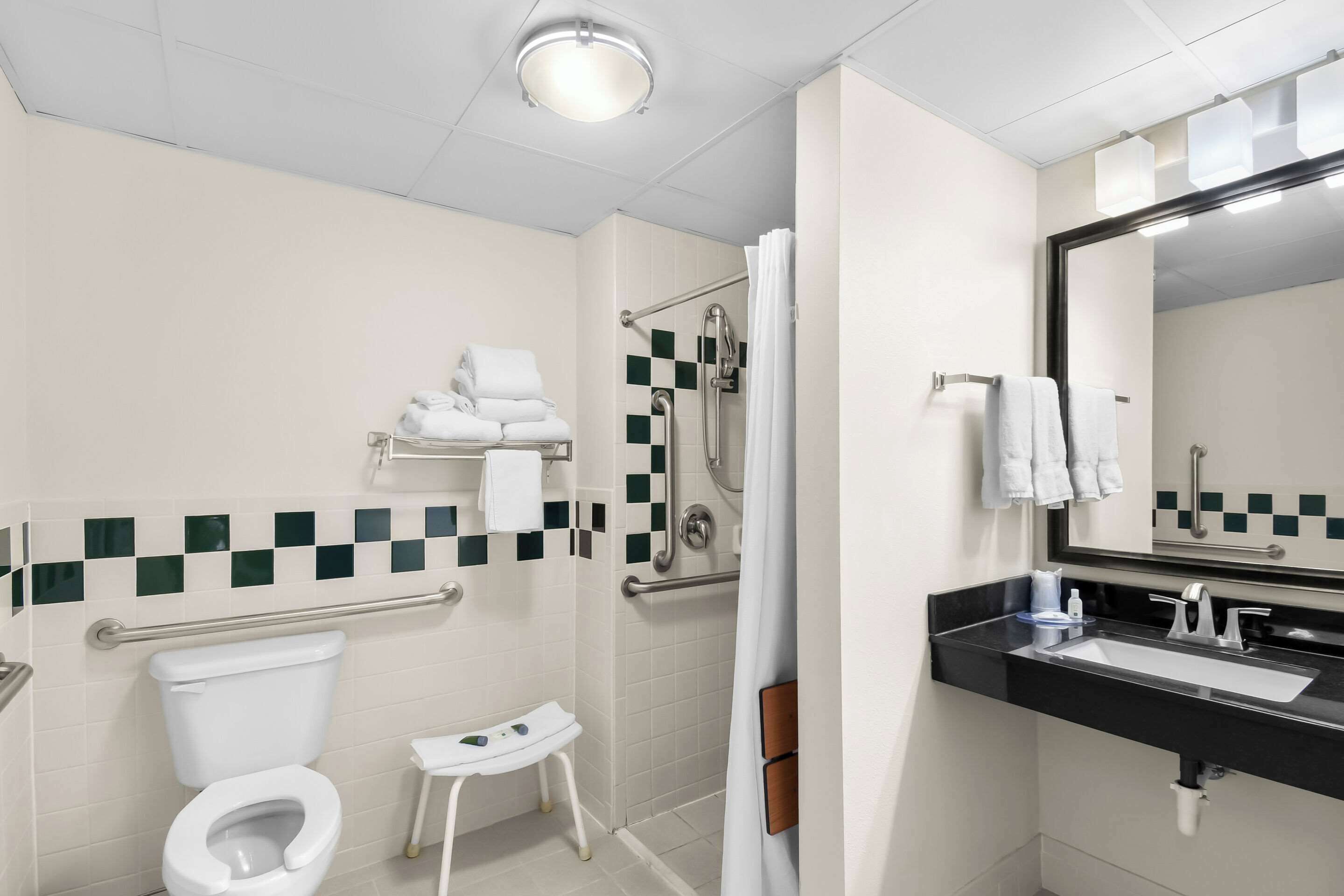 Un baño moderno con inodoro, ducha con puerta de vidrio, lavamanos y espejo, además de un pequeño taburete.