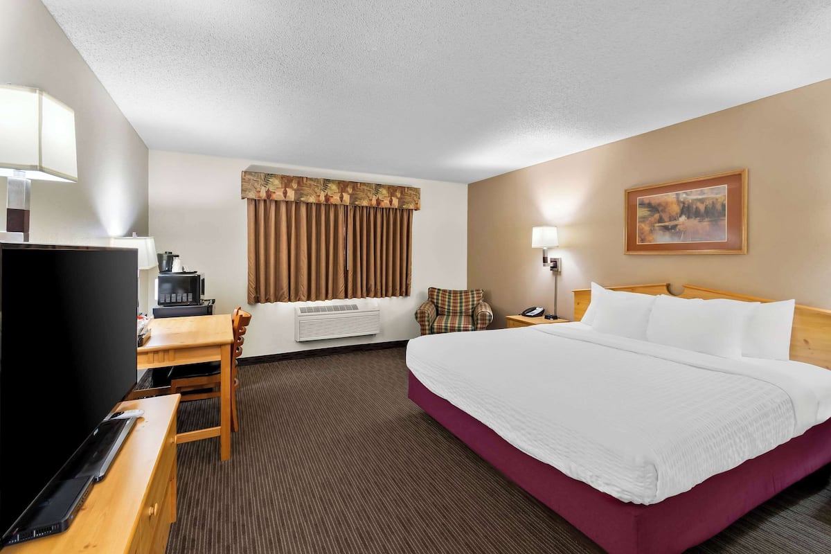 A hotel room with a large bed, a desk with a computer, a television, and a chair.