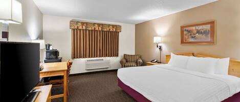 A hotel room with a large bed, a desk with a computer, a television, and a chair.