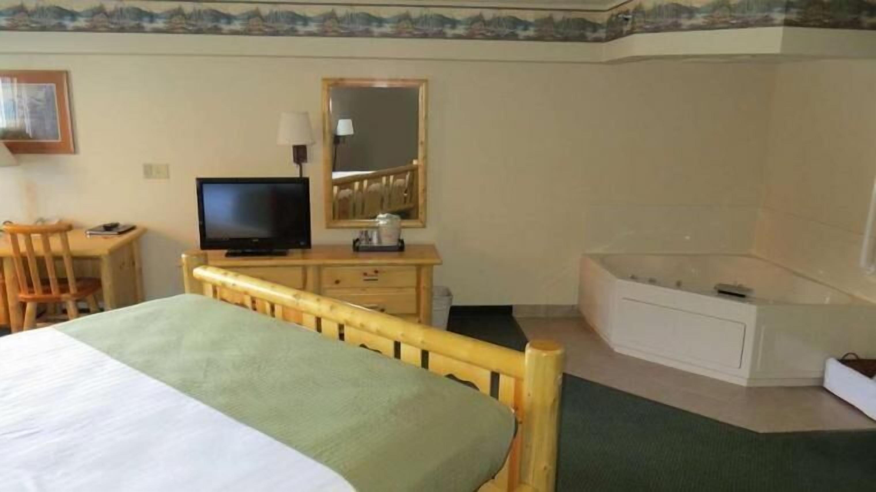 Una habitación de hotel con cama, escritorio, computadora, televisión, espejo y bañera.