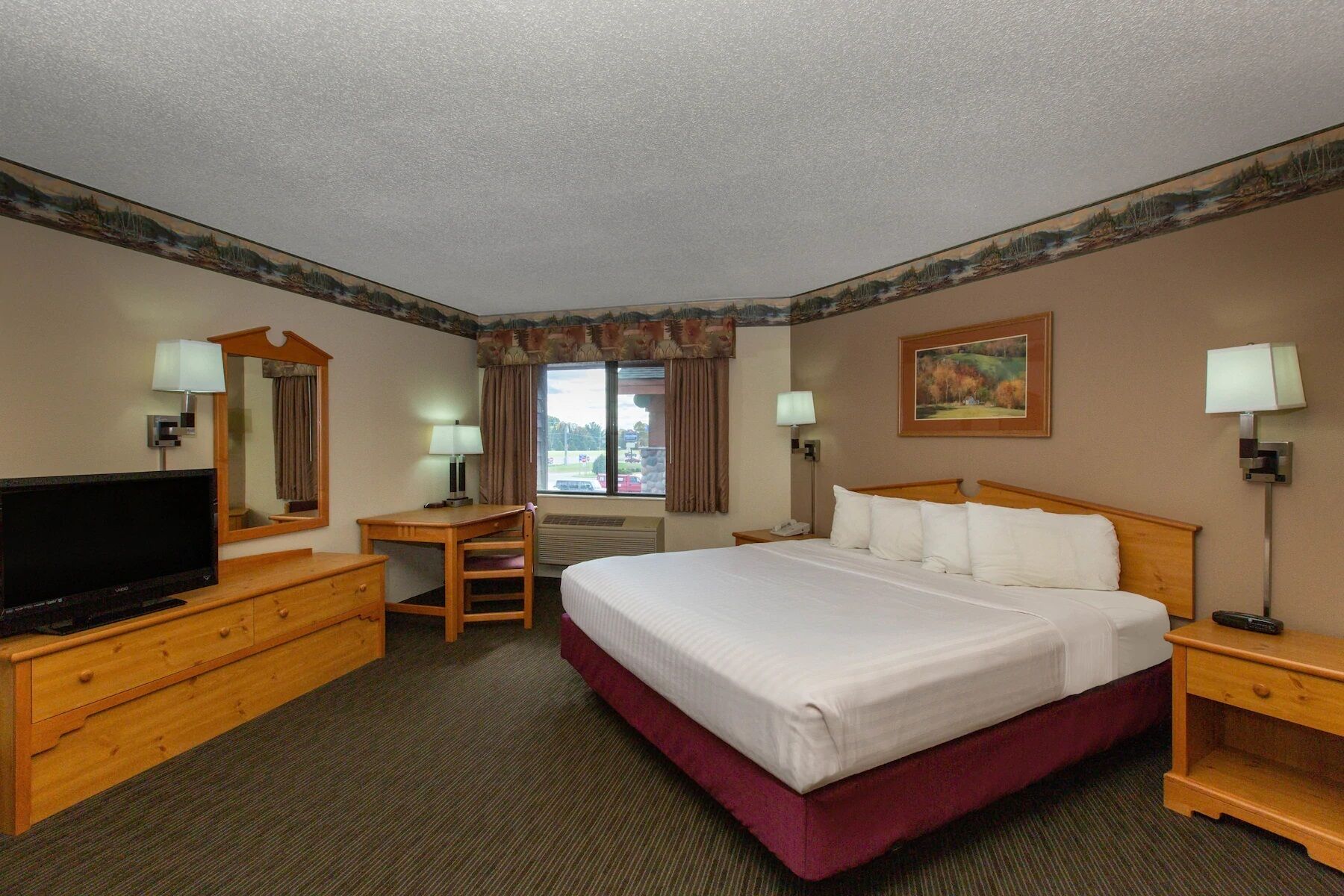 A hotel room with a large bed, a desk, a television, and a window with curtains.