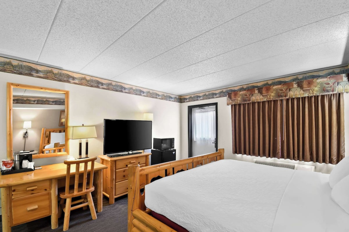 A hotel room with a bed, a desk with a chair, a television, a microwave, and a window with curtains.