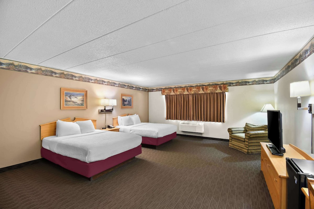 A hotel room with two beds, a television, a desk, and a chair.