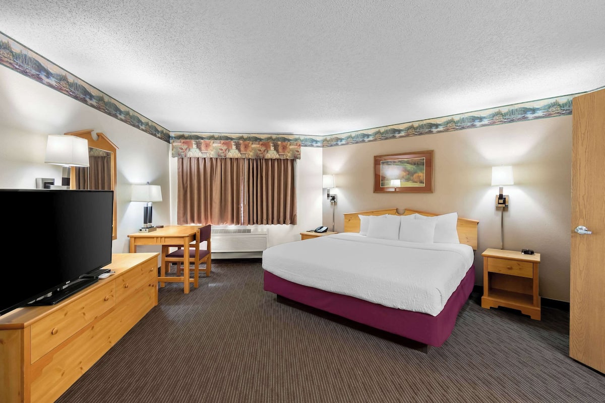 A hotel room with a bed, a desk, a television, and a window with curtains.