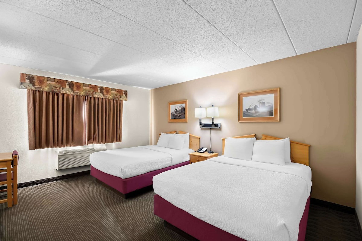 A hotel room with two beds, a desk, a chair, a lamp, and a picture on the wall.