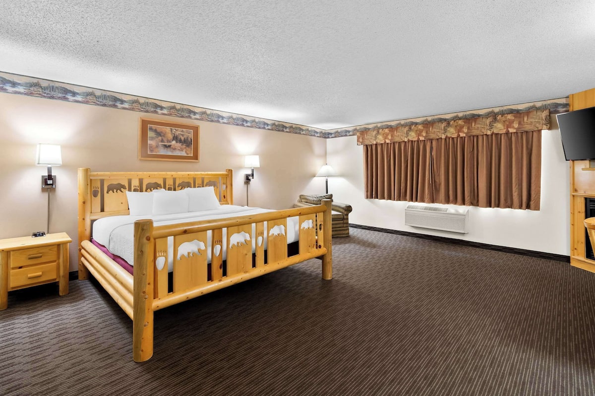 A hotel room with a wooden bed, bedside lamps, a flat-screen TV, and a large window with curtains.