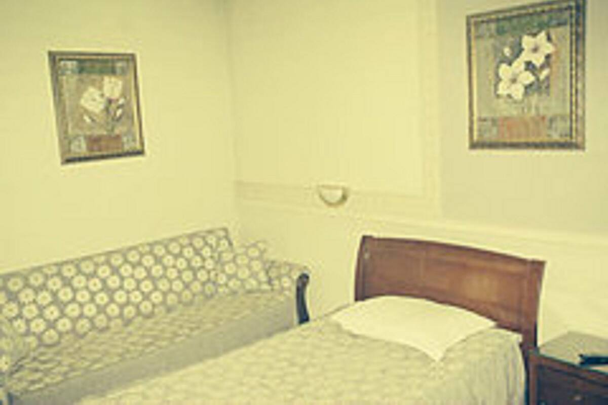 A bedroom with a patterned sofa, a wooden bed frame, and two framed artworks on the walls.