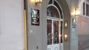 Een hotelentree met een bord waarop 'HOTEL DES PRINCES' staat, een decoratieve gebogen deuropening en wandlampen.