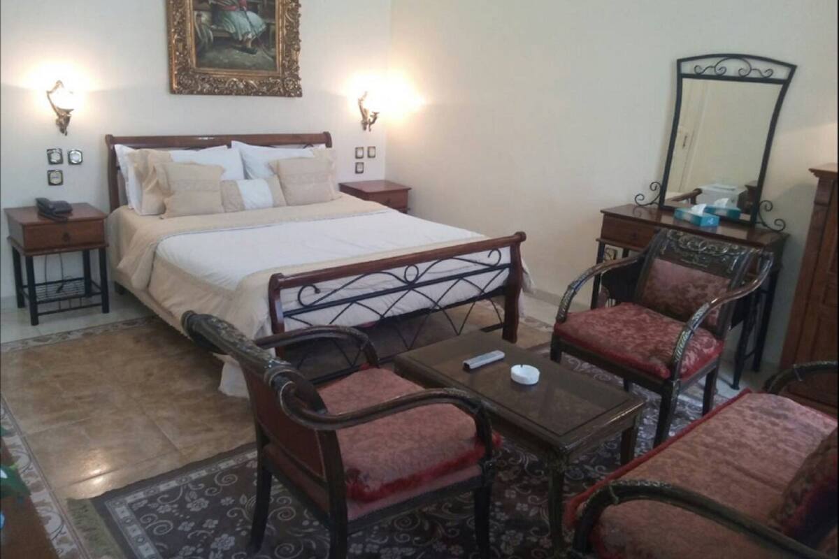 A bedroom with a large bed, two bedside tables, a nightstand, a mirror, and two chairs.
