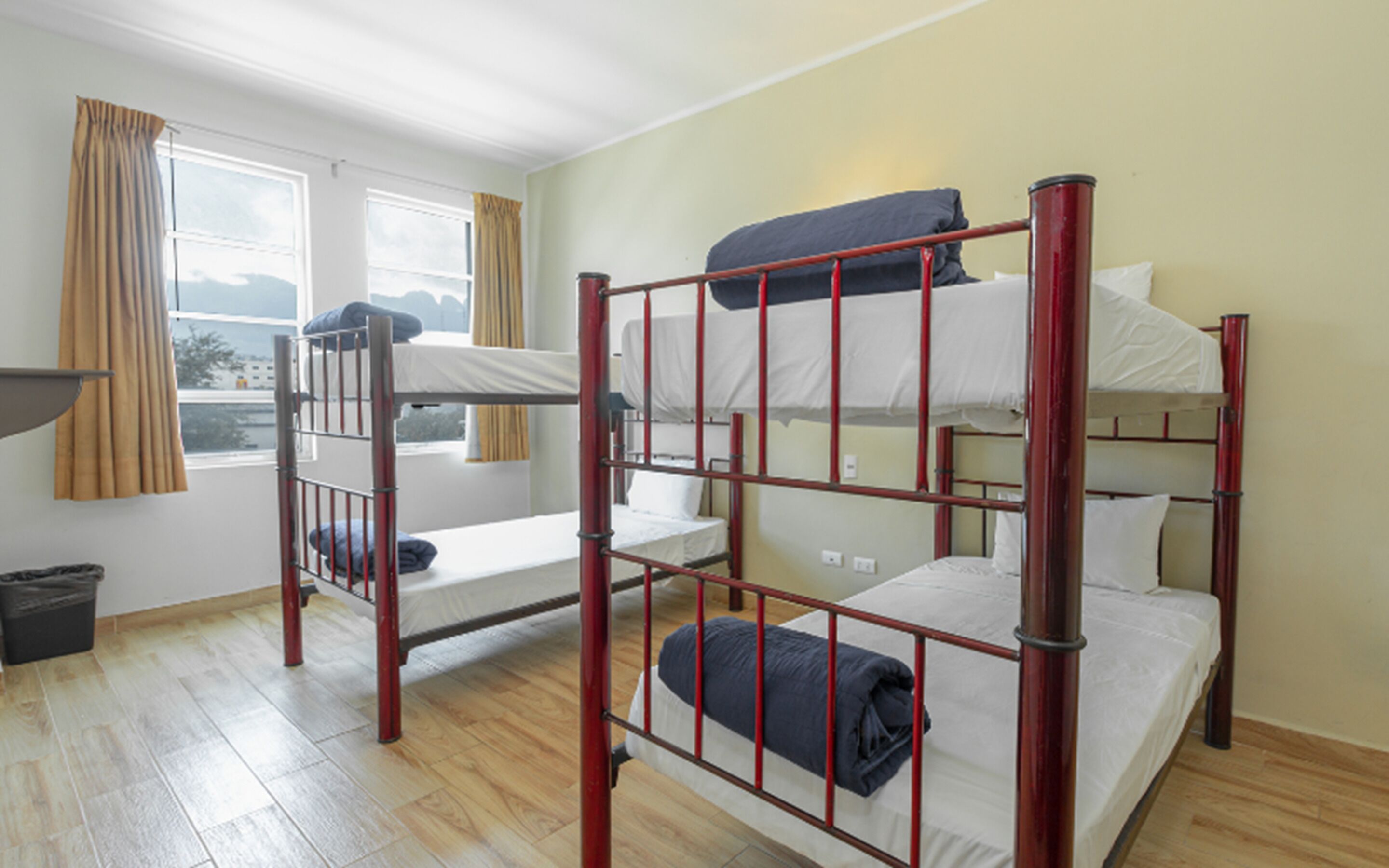 A dormitory room with bunk beds, a window with curtains, and a view of the outside.